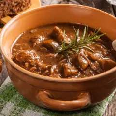 Aromatyczna zupa gulaszowa Ani gotuje się w glinianym naczyniu, ozdobiona gałązką rozmarynu. Obok kromki chleba.