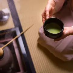 Rytuał parzenia herbaty po japońsku. Osoba w kimonie trzyma miseczkę z zieloną herbatą matcha, obok paruje czajniczek.