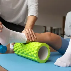 Fizjoterapeuta pomaga sportowcowi w automasażu łydki wałkiem, co jest kluczowe w klinicznej medycynie sportowej.