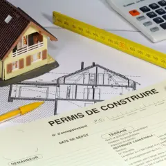 Maquette de maison, plans, mètre, calculatrice et formulaire "Permis de construire". La question : peut-on commencer les travaux pendant le recours des tiers ?
