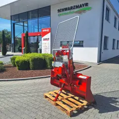 Roter Forstkran auf einer Palette vor einem Landtechnik-Gebäude. Ein robustes Gerät für den Einsatz im Wald, bereit für den Transport.