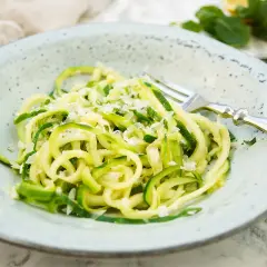 Ein Teller mit Zoodles, einem leichten Zucchini-Nudel-Gericht, bestreut mit Parmesan. Ein einfaches und gesundes Zoodles Rezept.