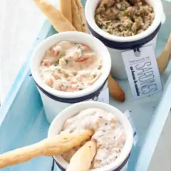 Trois ramequins de rillettes de la mer, dont une tartinade de sardines, présentés sur un plateau bleu avec des gressins.