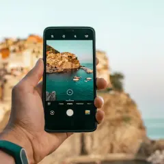 Dłoń trzyma smartfon z widokiem na malownicze miasteczko nad morzem. Dowiedz się, jak poprawić zdjęcie w telefonie, by uchwycić takie piękno.