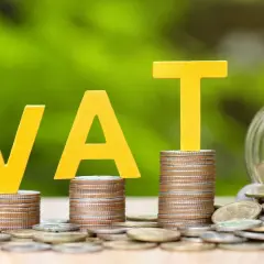 Żółte litery VAT na stosach monet, obok słoik pełen pieniędzy. Grupa vat to ważny element finansów.