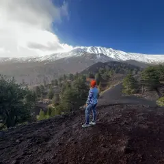 Kobieta w pomarańczowej czapce podziwia majestatyczny wulkan Etna pokryty śniegiem.