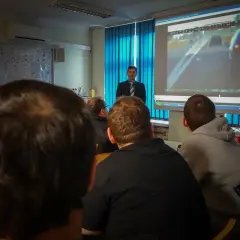 Uczestnicy kursu reedukacyjnego oglądają film z jazdy samochodem na ekranie.