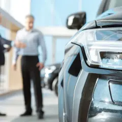 Elegancki czarny samochód w salonie. Dwóch mężczyzn w tle omawia, co można wziąć w leasing.