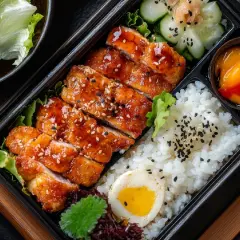 A delicious hinomaru bento with teriyaki chicken, rice, a hard-boiled egg, cucumber salad, and a sweet fruit topping.