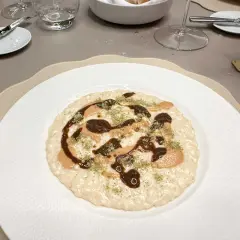 Un risotto cremoso con salse scure e chiare, guarnito con erbe verdi. Andrea la Rossa lo ha preparato con cura.