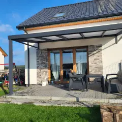 Nowoczesna pergola z poliwęglanowym dachem chroni taras z meblami. Idealne miejsce na relaks.