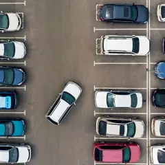 Widok z góry na parking z wieloma samochodami. Jeden biały samochód jest zaparkowany pod kątem, co wymaga korekty.