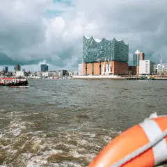 Blick vom Wasser auf Hamburgs Elbphilharmonie und die Skyline. Eine kleine Barkasse fährt vorbei. Welche Hafenrundfahrt in Hamburg ist die beste?