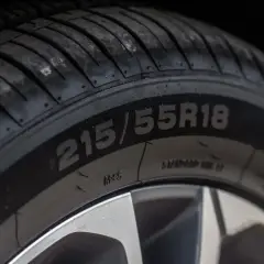 Zbliżenie na oponę z widocznym rozmiarem 215/55R18. Na boku opony można dostrzec oznaczenia dotyczące daty produkcji.