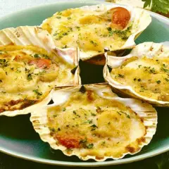 Quattro capesante gratinate, un delizioso antipasto di pesce, servite in conchiglia con erbe aromatiche.