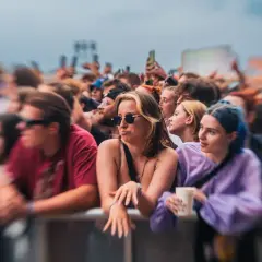 Tłum ludzi na koncercie Męskie Granie, z widocznymi twarzami w pierwszym planie.
