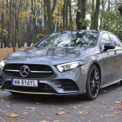 Szary hatchback Mercedes Klasa A zaparkowany na chodniku wśród jesiennych liści.