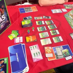 Gra planszowa The Sims w akcji. Widać pudełko, karty akcji, karty domów i planszę. Premiera The Sims Board Game zapowiada się świetnie!