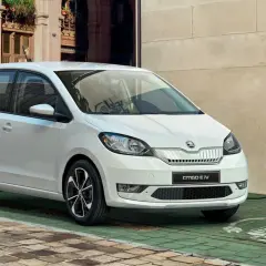 Biały Skoda Citigo e IV ładuje się przy stacji ładowania na brukowanej uliczce, gotowy na miejskie przygody.