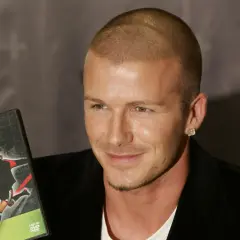 David Beckham, con su característico corte afeitado, sonríe mientras sostiene un DVD de sus habilidades de fútbol.