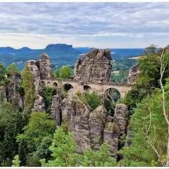 Kamienny most Bastei w górach Saksonii, łączący skalne baszty pośród zielonych lasów i malowniczych krajobrazów.