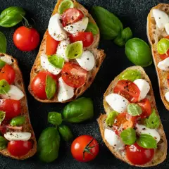 Chrupiące grzanki z pomidorami i mozzarellą, ozdobione świeżą bazylią. Idealna przekąska na lato.