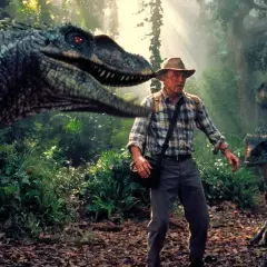 Człowiek w kapeluszu otoczony przez groźne welociraptory w dżungli. Scena z filmów "Park Jurajski".