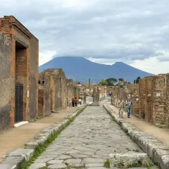 Antigua calle empedrada en el parque arqueológico de Pompeya, con ruinas a ambos lados y el Vesubio al fondo.