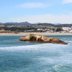 Olas rompen en la playa de Barreiros, con una roca en primer plano y el pueblo al fondo.