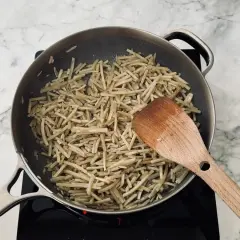 Strips of burdock root are being stir-fried in a pan, a key step in preparing a delicious kinpira recipe. A wooden spatula is used to toss the ingredients.
