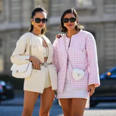 Dos mujeres lucen conjuntos de tweed, uno blanco y otro rosa, encarnando la moda preppy con bolsos a juego y gafas de sol.