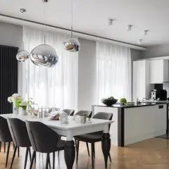 Elegancki styl glamour salon z kuchnią. Nowoczesne lampy, biała wyspa kuchenna i stół z szarymi krzesłami tworzą spójną całość.