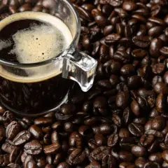 Una taza de café oscuro con espuma, rodeada de granos de café tostados. Dicen que el café es afrodisiaco, ¿será cierto?