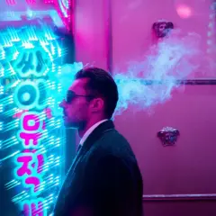 Man exhales smoke in front of vibrant neon signs, a cool example of led light photography ideas.
