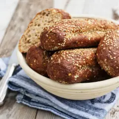 Koszyk z ciemnym chlebem posypanym sezamem i kromka chleba na drewnianym tle.