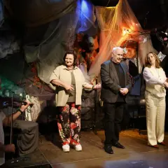 W piwnicy pod baranami skład: skrzypek, dwie kobiety i mężczyzna na scenie. Tło tworzą tkaniny i dekoracje.