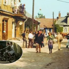 Scena z filmu "Znachor" kręcona w malowniczej wsi. W tle drewniane domy, a na pierwszym planie para na motocyklu.