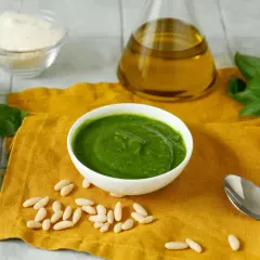 Pesto fresco in una ciotola bianca, con ingredienti per una ricetta pesto semplice: basilico, pinoli, olio d'oliva e parmigiano grattugiato.