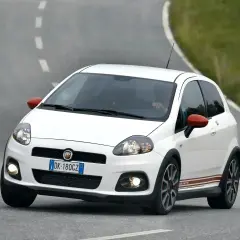 Biały Fiat Punto Evo Abarth z czerwonymi lusterkami pędzi po zakręcie na asfaltowej drodze.