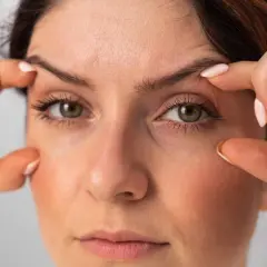 Dita che sollevano la pelle per mostrare come truccare gli occhi con palpebre cadenti, creando un effetto lifting.
