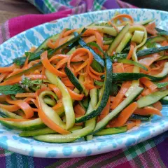 Deliziose zucchine alla julienne con carote, guarnite con menta fresca, servite su un piatto colorato.