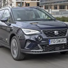 Ciemnogranatowy Seat Arona FR jedzie ulicą. Kierowca w okularach prowadzi auto.