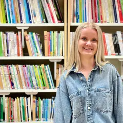 Evelina Persson ler glatt framför bokhyllor fyllda med färgglada böcker.