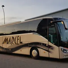 Autobus Marcel z napisem na boku, stojący na parkingu, z zielonymi flagami w tle.