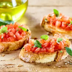 Trzy chrupiące kromki pieczywa, obficie posypane posiekanymi pomidorami i listkami bazylii. To klasyczna bruschetta włoska, gotowa do skropienia oliwą.