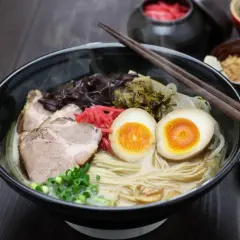 Pyszny ramen co to? Miska parującego bulionu z makaronem, plastrami wieprzowiny, jajkiem na pół, szczypiorkiem i marynowanymi dodatkami.