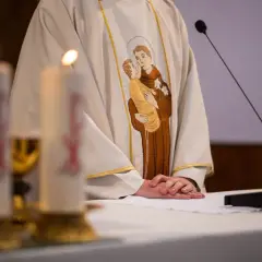 Szczegół szaty kapłańskiej z haftem świętego z dzieckiem, świece i mikrofon.