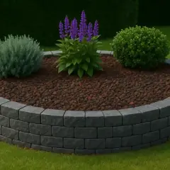 Aiuola circolare con bordura in pietra grigia, riempita di corteccia e piante verdi con fiori viola.
