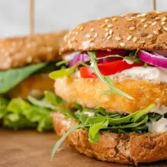 Pyszny burger z krewetkami, chrupiącą sałatą, pomidorem i czerwoną cebulą, polany kremowym sosem.