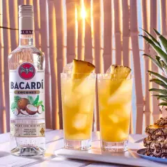Butelka Bacardi Coconut obok dwóch drinków z ananasem i cała ananasowa piramidka. Idealne na tropikalne przyjęcie!